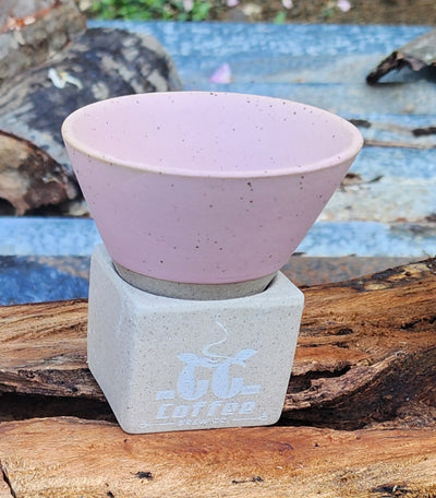 Pink conical ceramic coffee cup with Japanese-style coarse base on wooden surface.